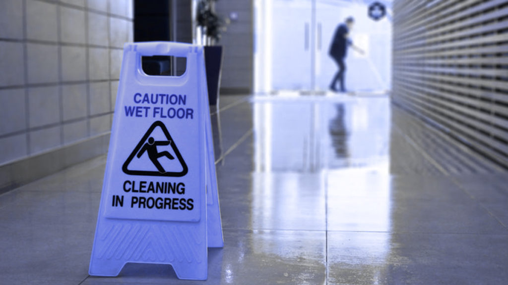 A "Cleaning in Progress" sign and a worker mopping the floor so no one is injured.